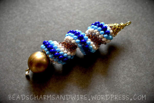 A beaded keychain ornament in the shape of a grooved helix, with blue, cream, and brown-hued beads.