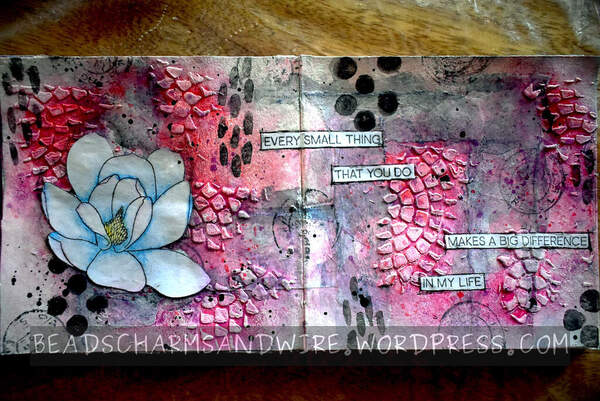 An art journal spread over 2 square pages. The pink-and-gray background is made of partial, concentric, stone-like textures and black stamp markings. On the left page is a pale-blue and white flower.