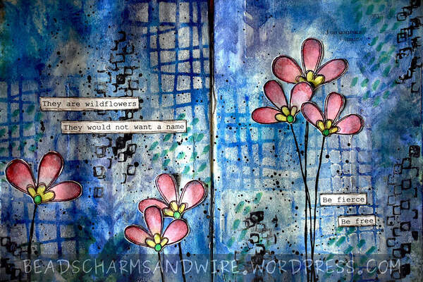 An art journal spread over 2 pages. The background is blue with areas of dark blue and white from stencil textures. Pink and yellow wildflowers form the focal elements.